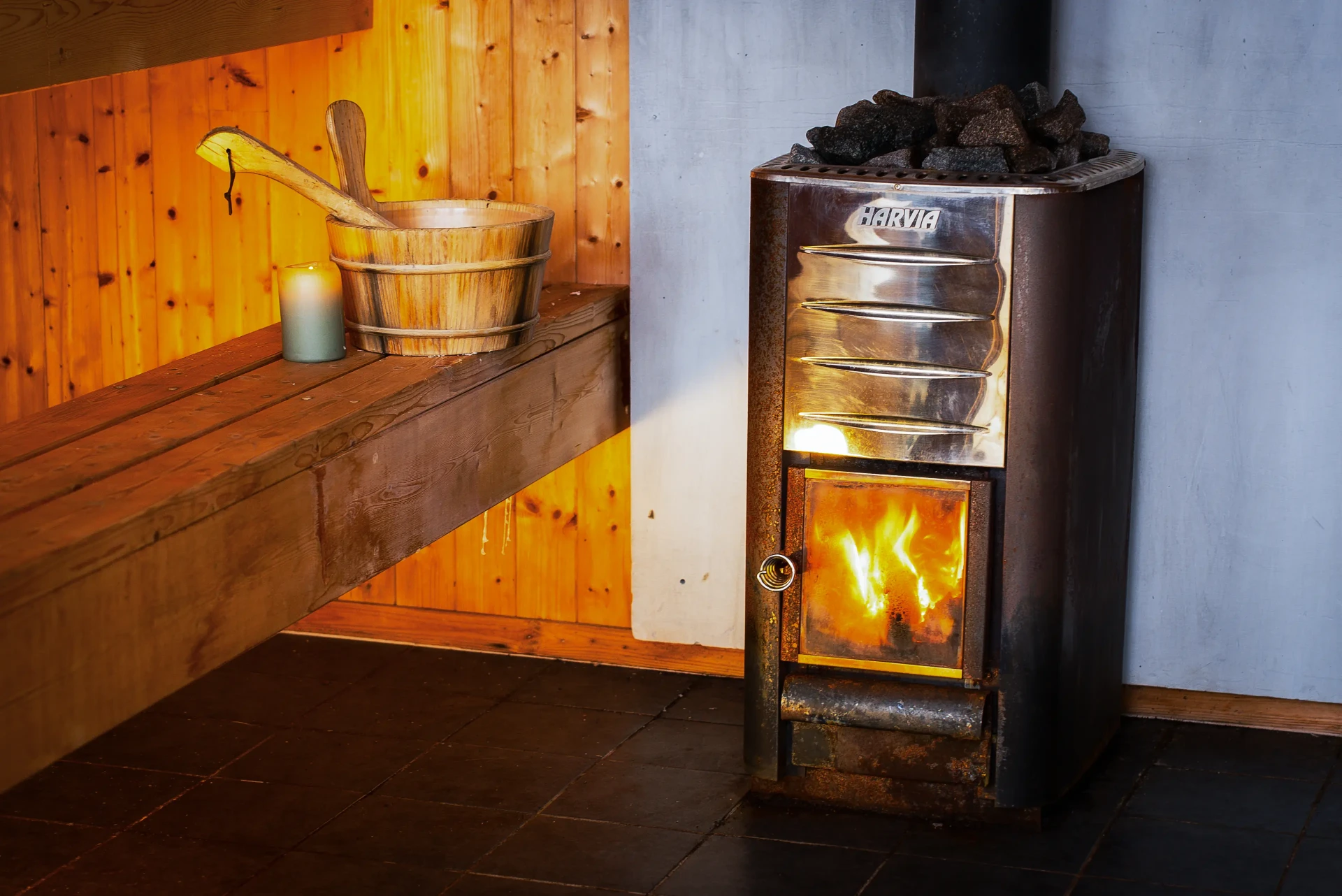 Wood-fired Harvia sauna stove burning bright beside pine bench and water bucket