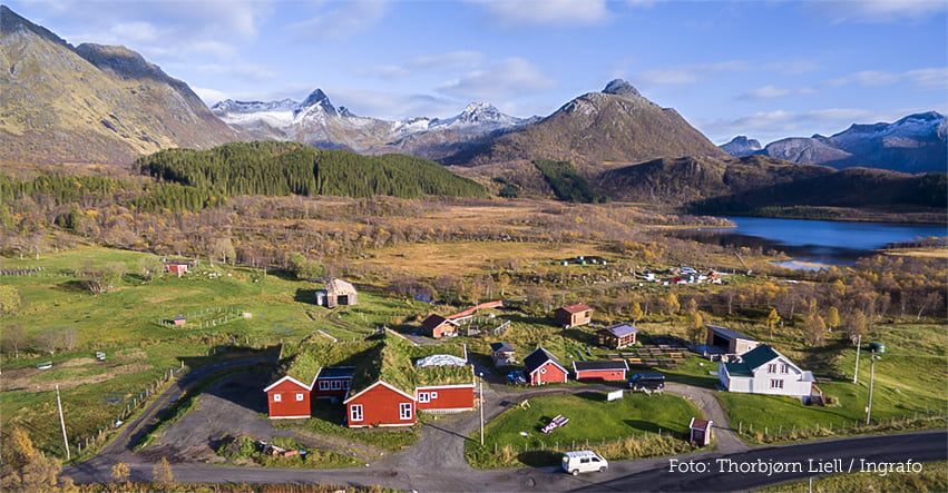 Aerial autumn view of the Livland farmstead with red cabins, lake and Lofoten peaks beyond