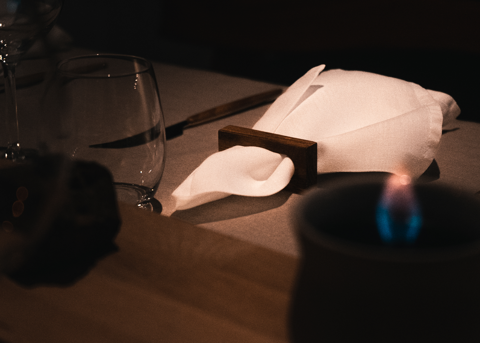 Intimate table setting with linen napkin, wine glass and open flame in low candlelight