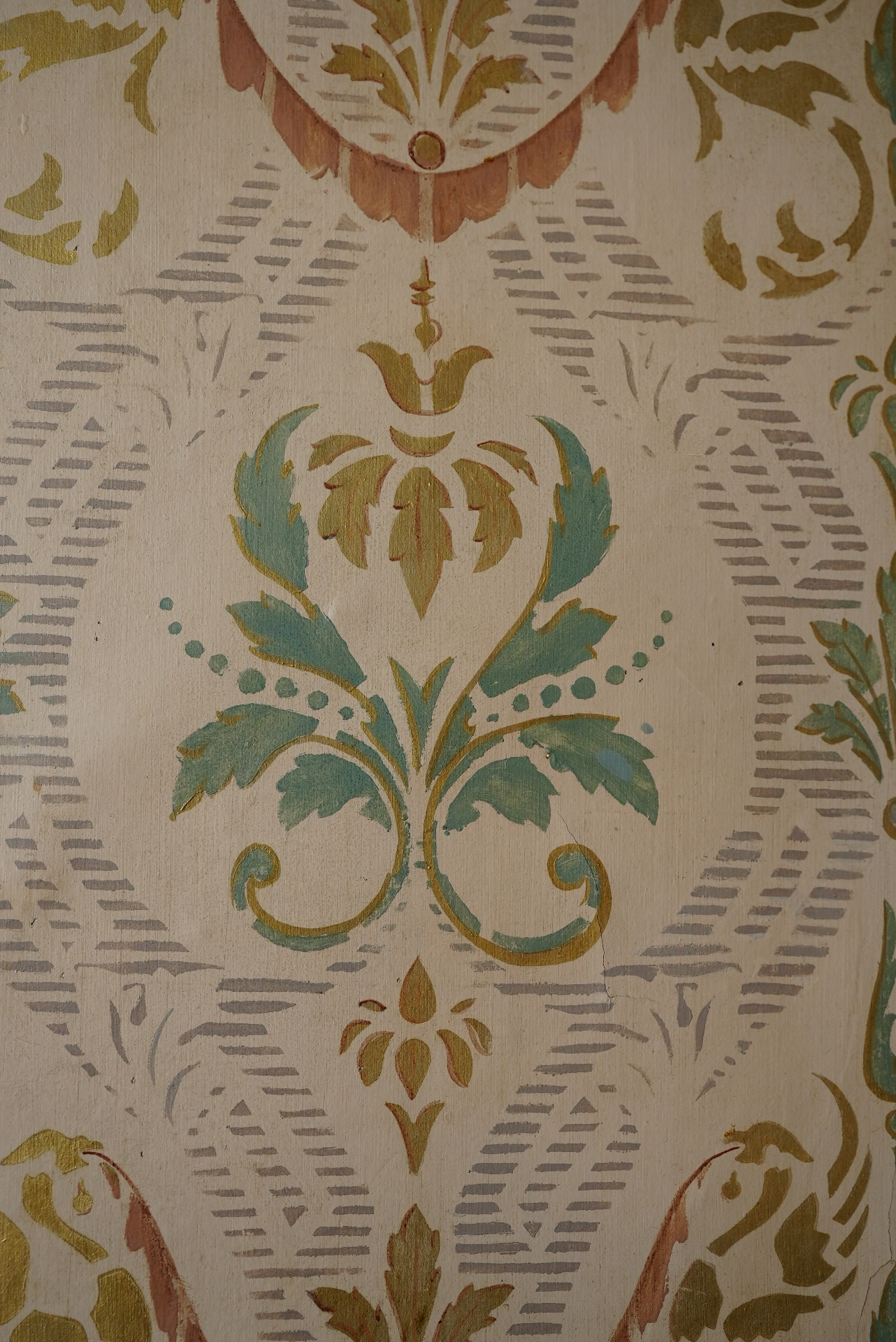 Close study of hand-painted floral wall decoration in muted copper, sage and grey on old timber