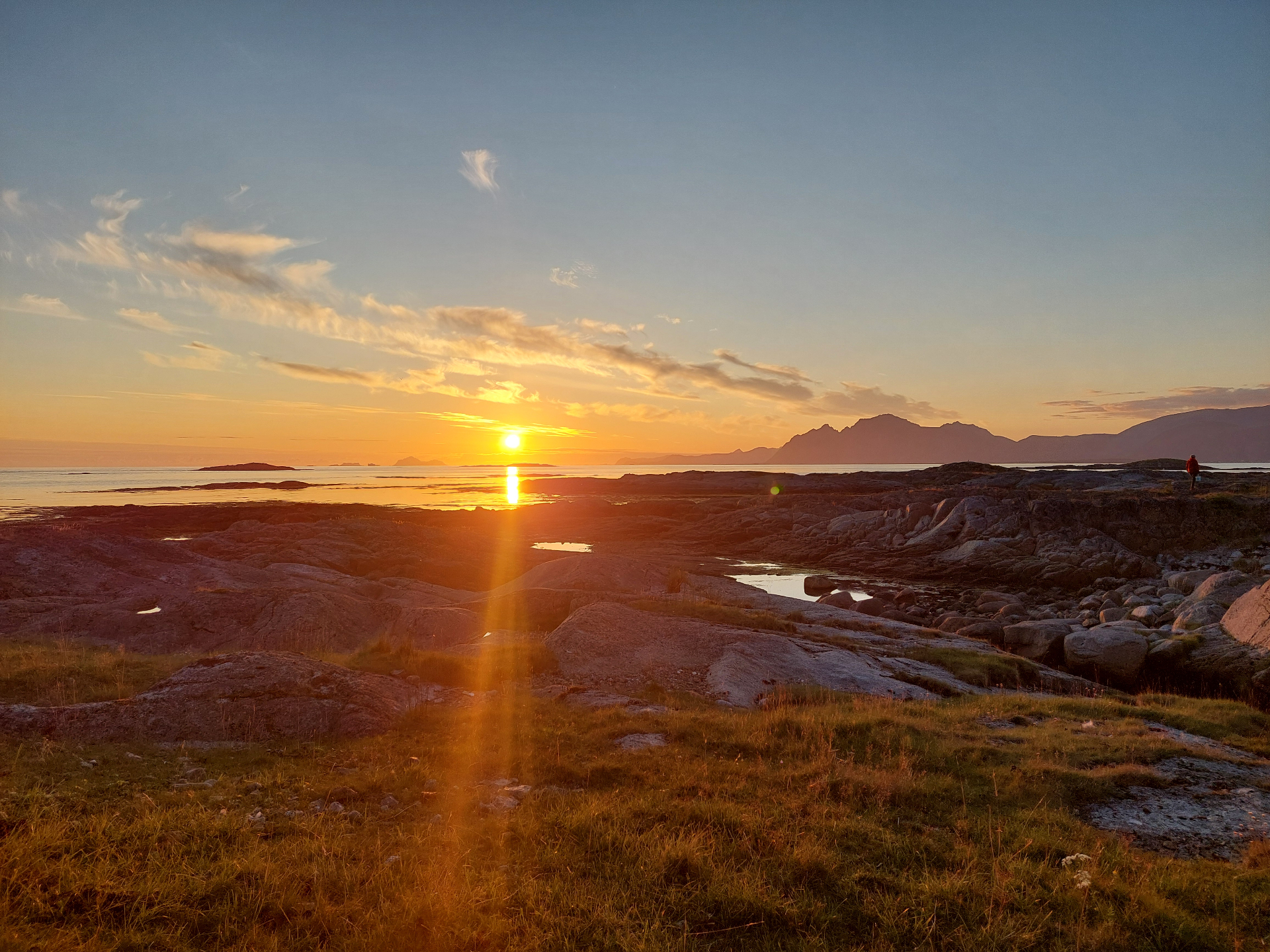 Golden midnight sun reflecting across tidal flats and smooth coastal rock under a pale evening sky