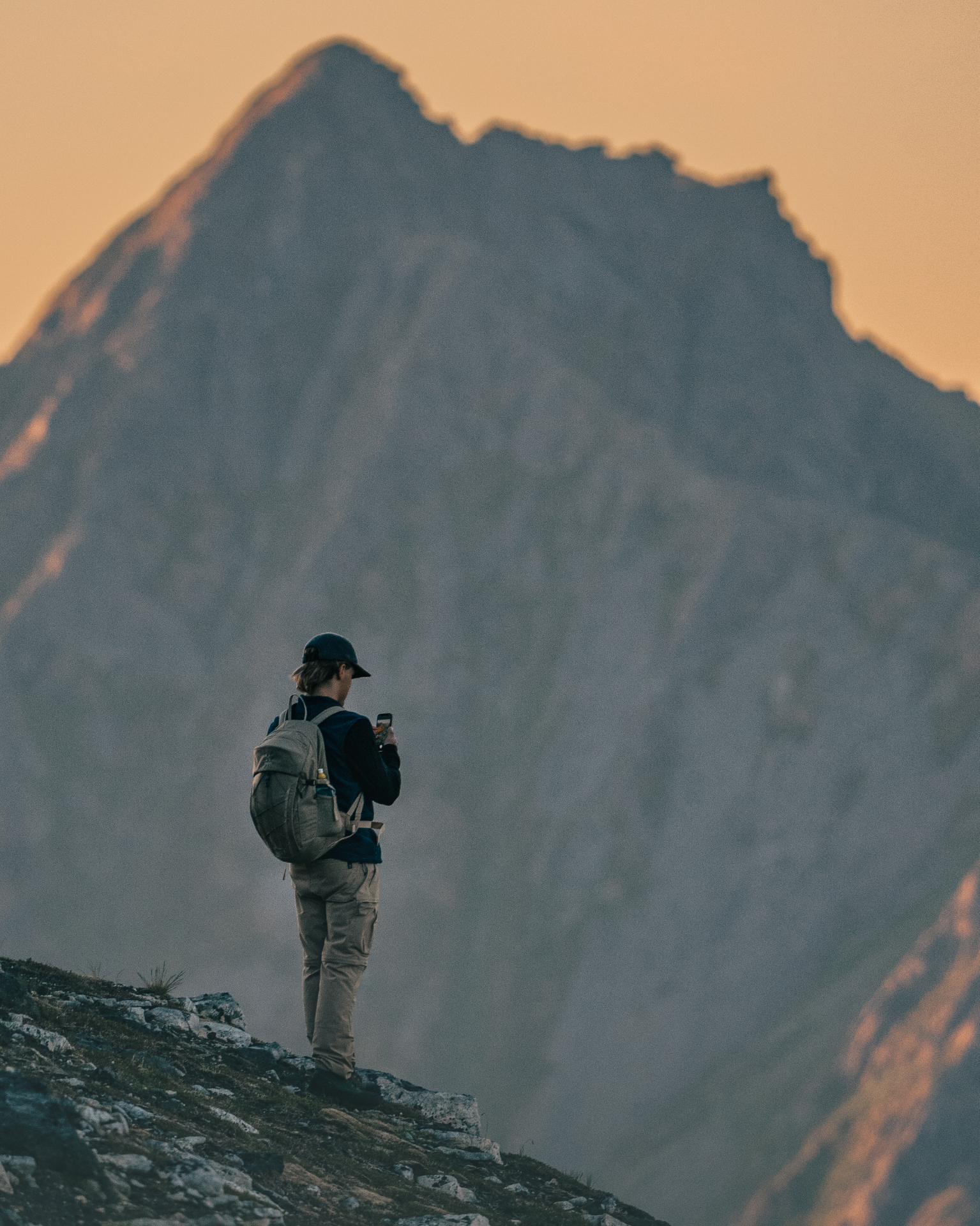 Lone hiker on a ridge before a towering peak in warm summer dusk light