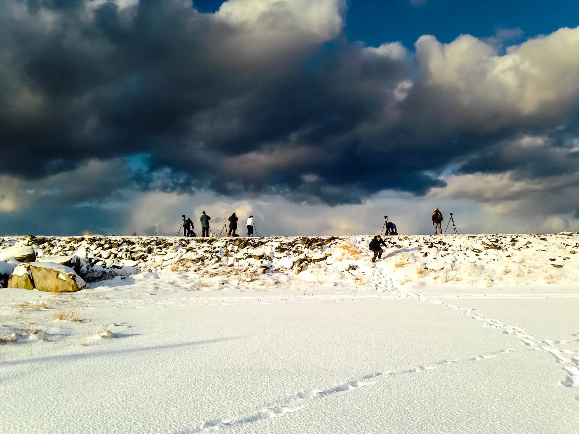Small group of photographers standing on a snowy ridge beneath towering storm clouds