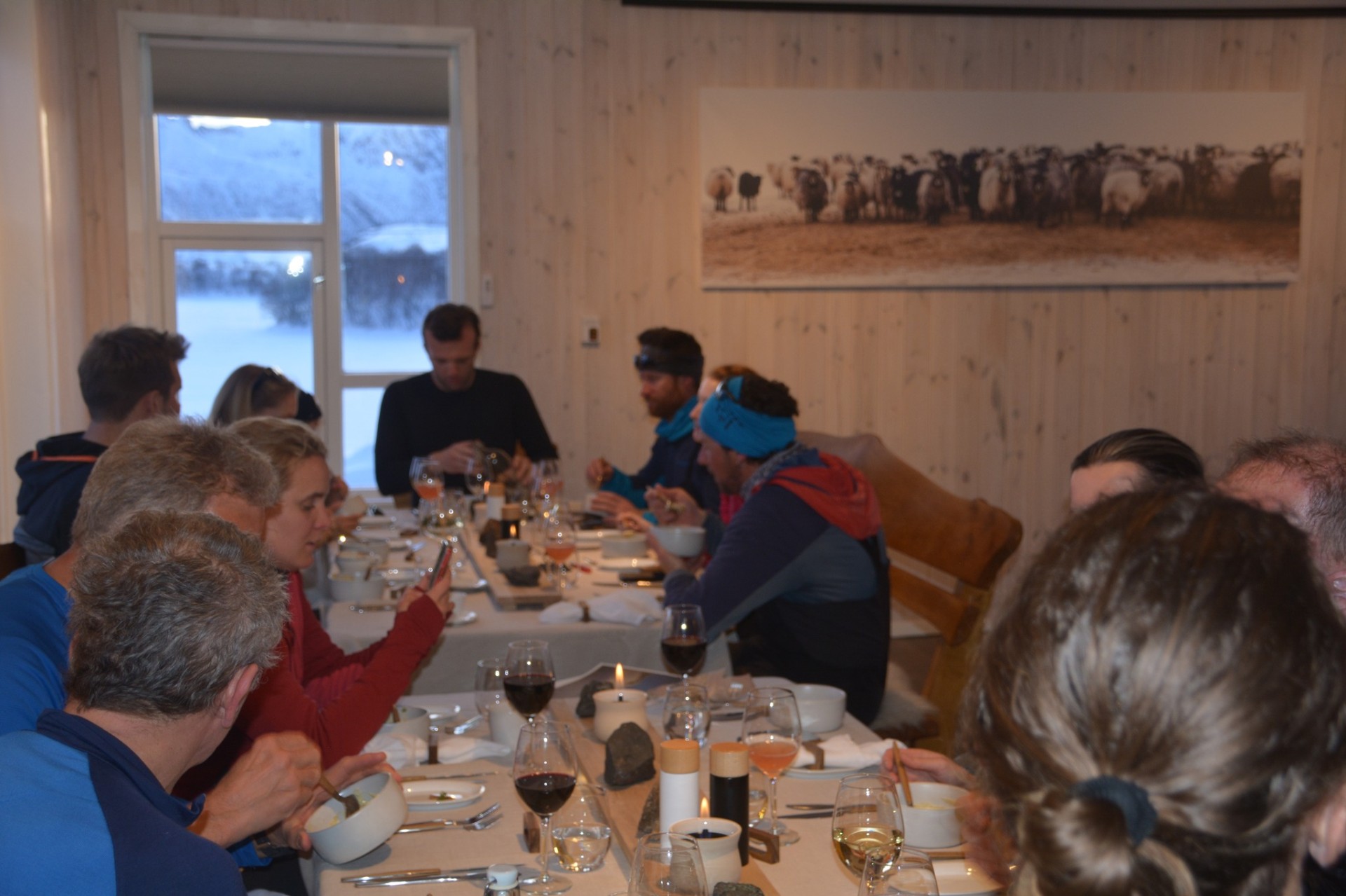 Guests gathered around a candlelit communal dinner table with snow outside the window
