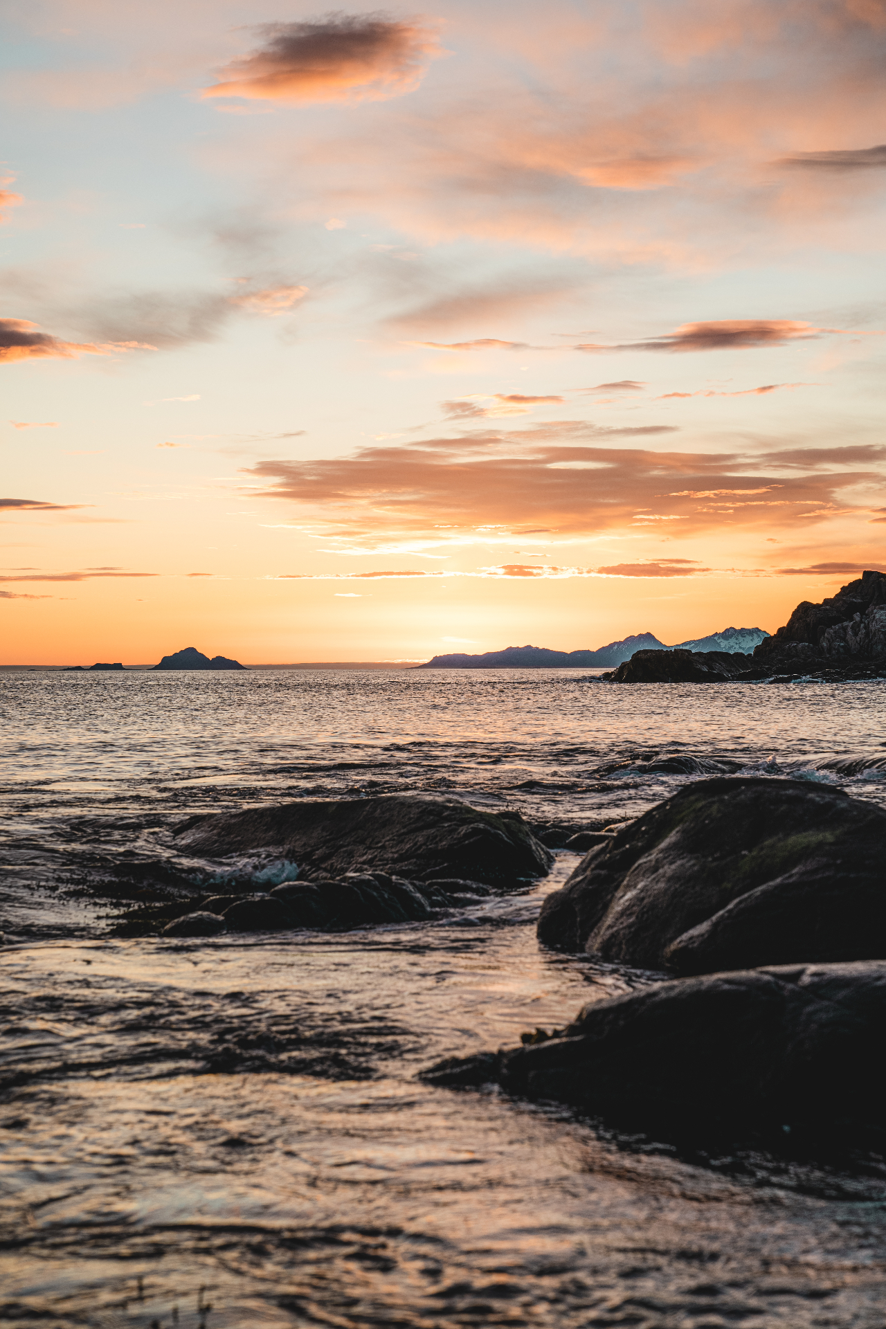 Rocky Lofoten shoreline in soft pastel sunset with distant islands on the horizon