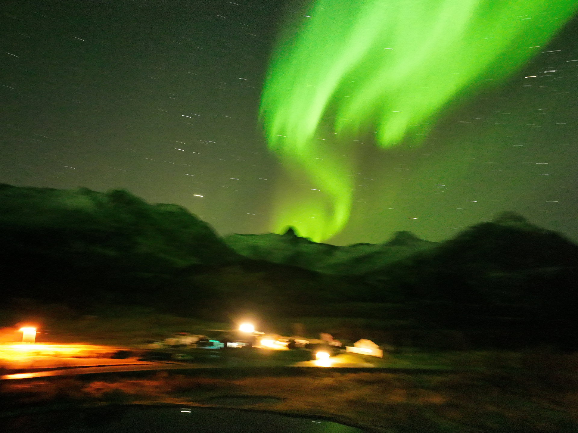 Aerial view of a Lofoten village at night with a swirling green aurora above dark peaks