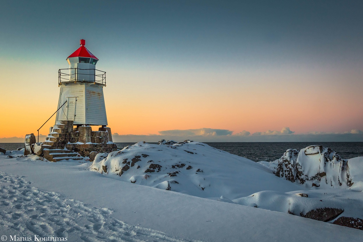 Red-capped lighthouse on snow-covered rocks at pastel winter dusk
