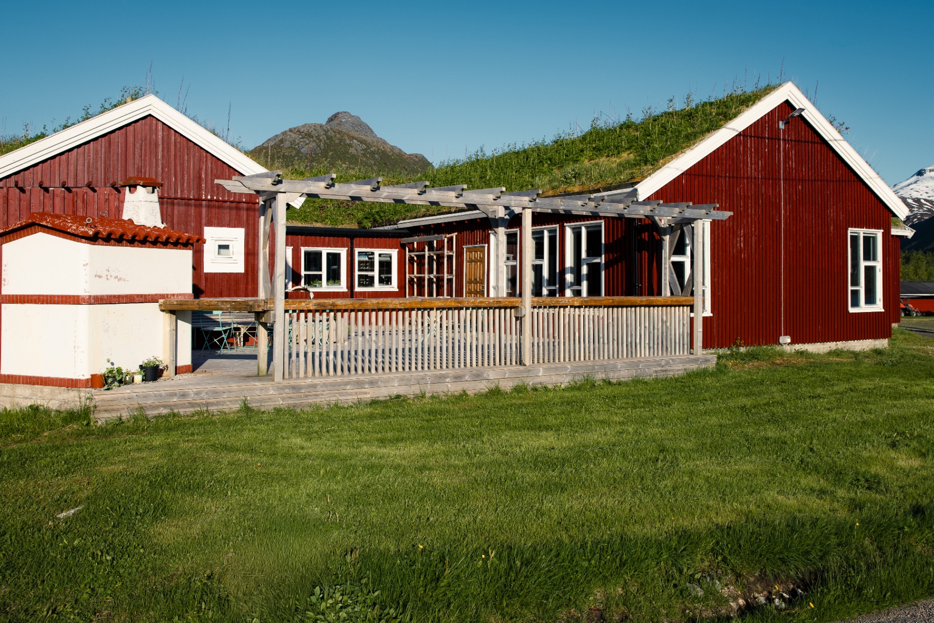 Wide exterior of red turf-roof cabins and terrace set against Lofoten mountains