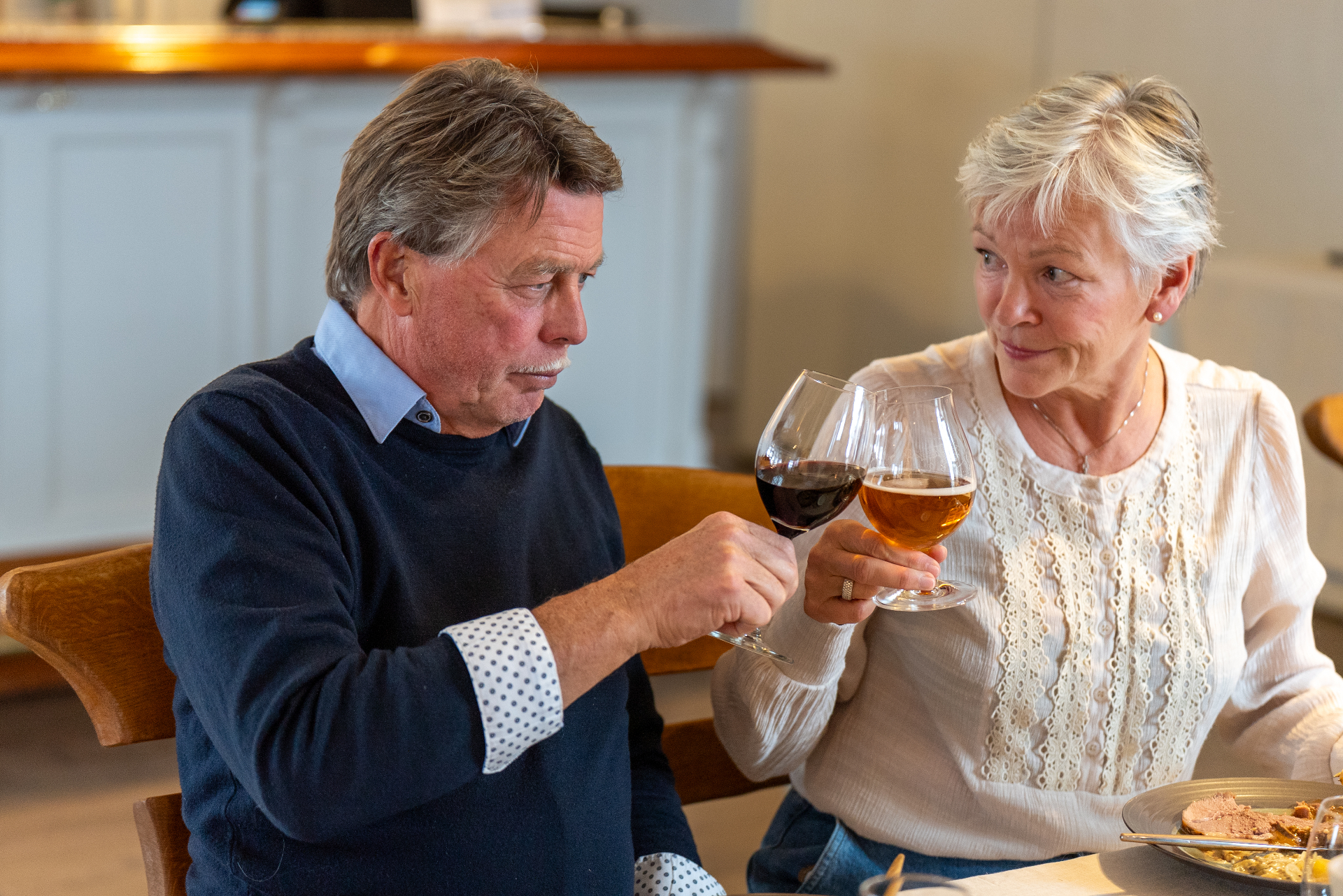 A couple raising a glass of red wine and beer in a warm toast at the table