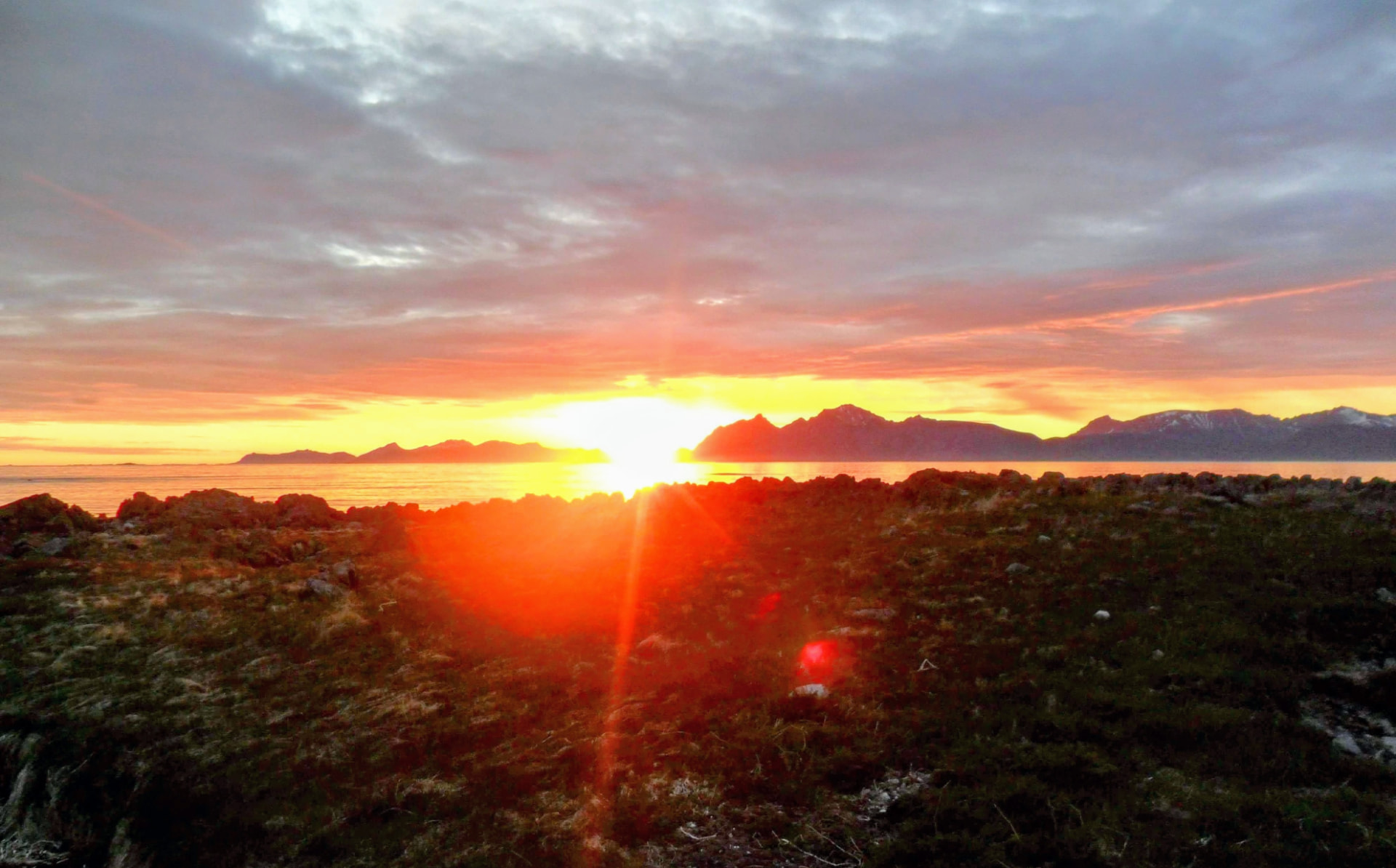 Low midnight sun flaring over the sea from Engøya with mountains silhouetted on the horizon