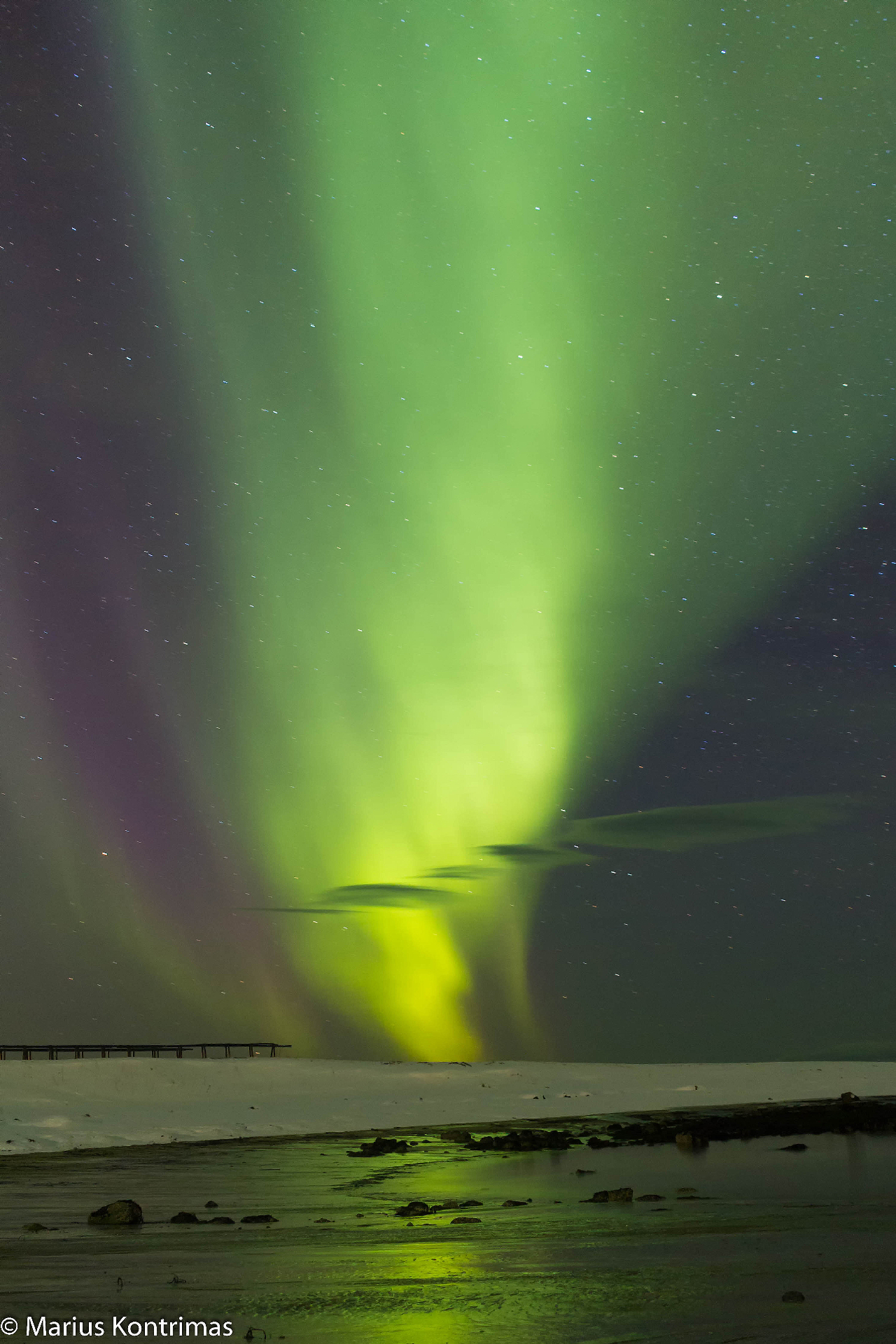 Vertical pillar of green and yellow aurora over a frozen shore