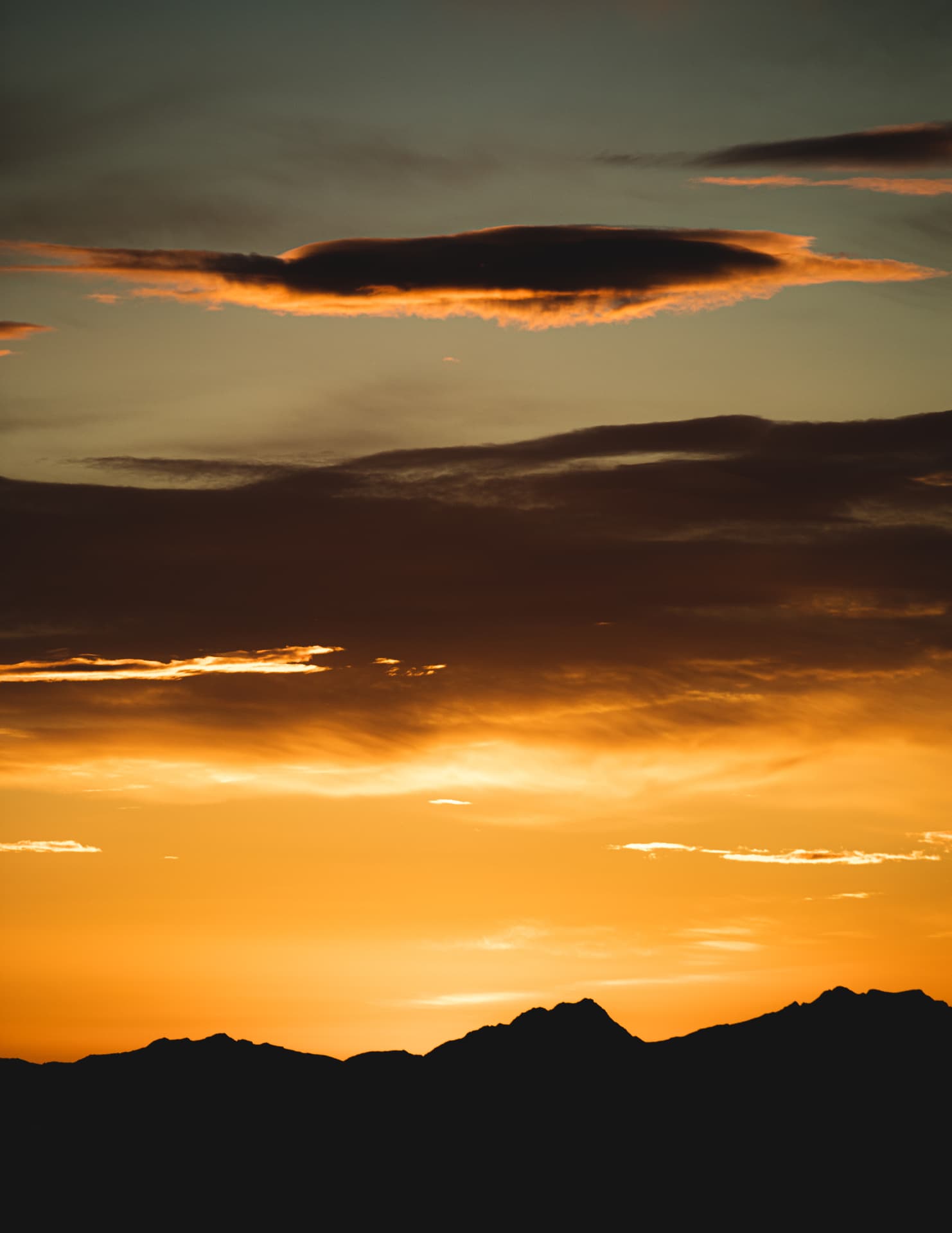 Lenticular cloud above a silhouetted mountain ridge under a copper sunset sky