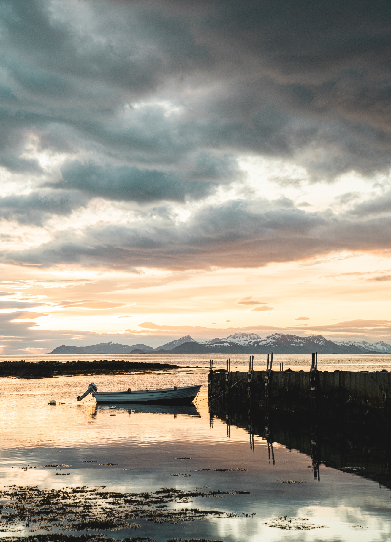 Small boat moored in a quiet harbour at luminous evening with distant snowy mountains