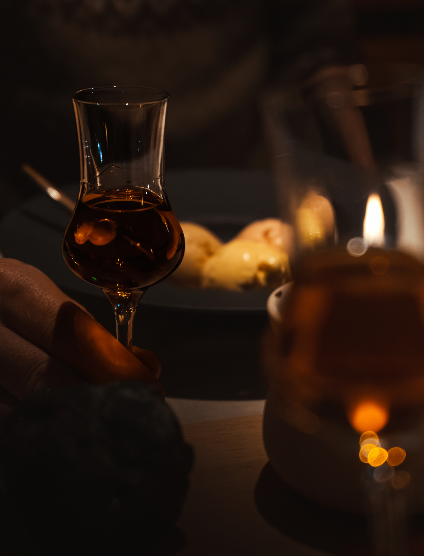 Hand holding a glass beside a candle flame in a dark Nordic room — quiet, low-impact hospitality at VISDI