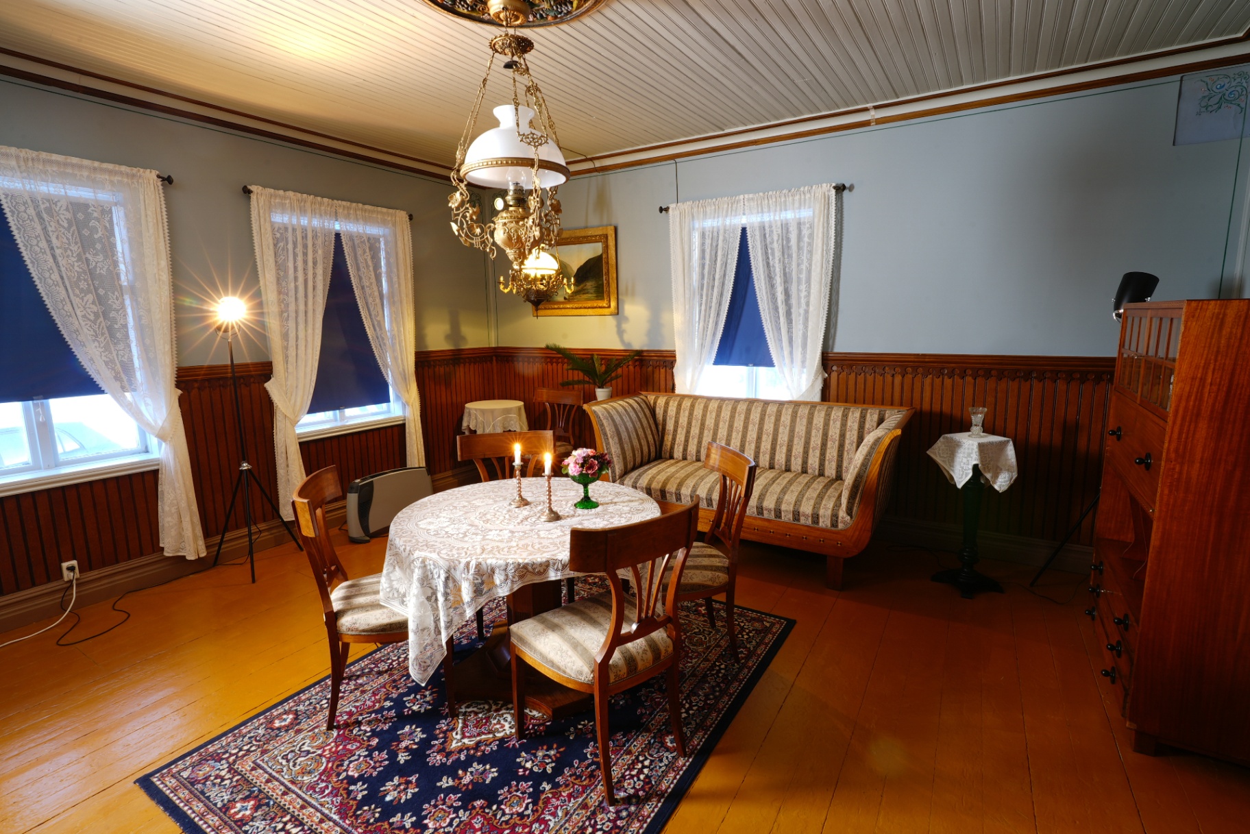 Historic sitting room with lace curtains, painted walls, brass lamp and upholstered sofa