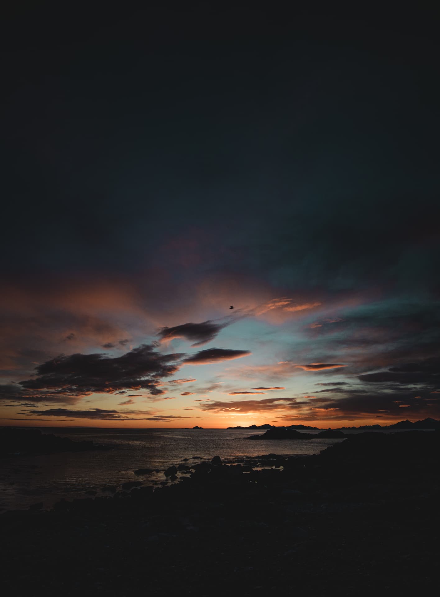 Deep blue and copper afterglow above a silhouetted Arctic shoreline