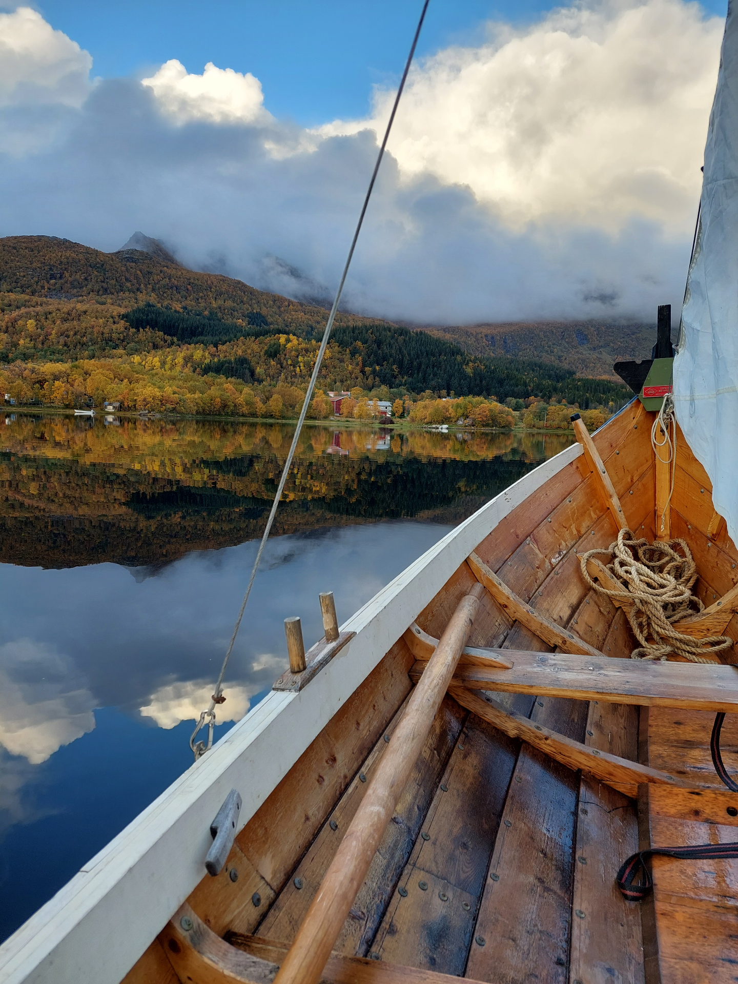 Inside a traditional wooden Nordlandsbåt on mirror-still autumn water with mountain reflections beyond