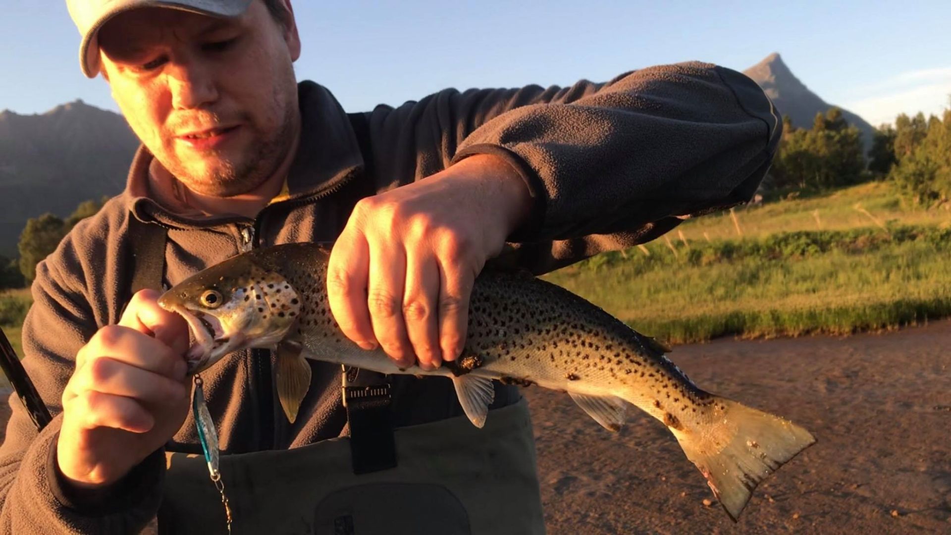 Angler in waders holding a large speckled sea trout in warm midnight-sun light