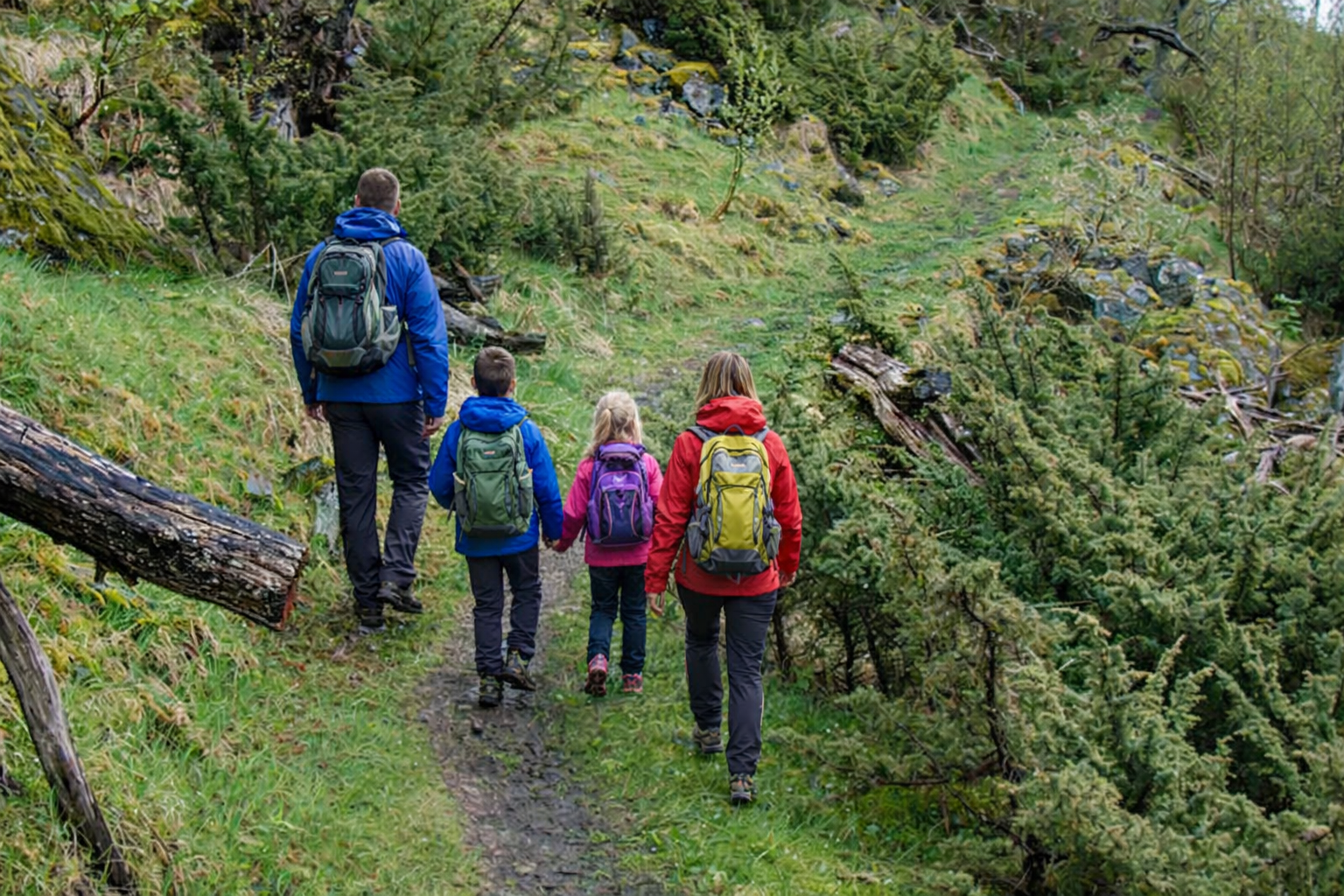 Family of four hiking a mossy forest trail into Rangeldalen with colourful packs