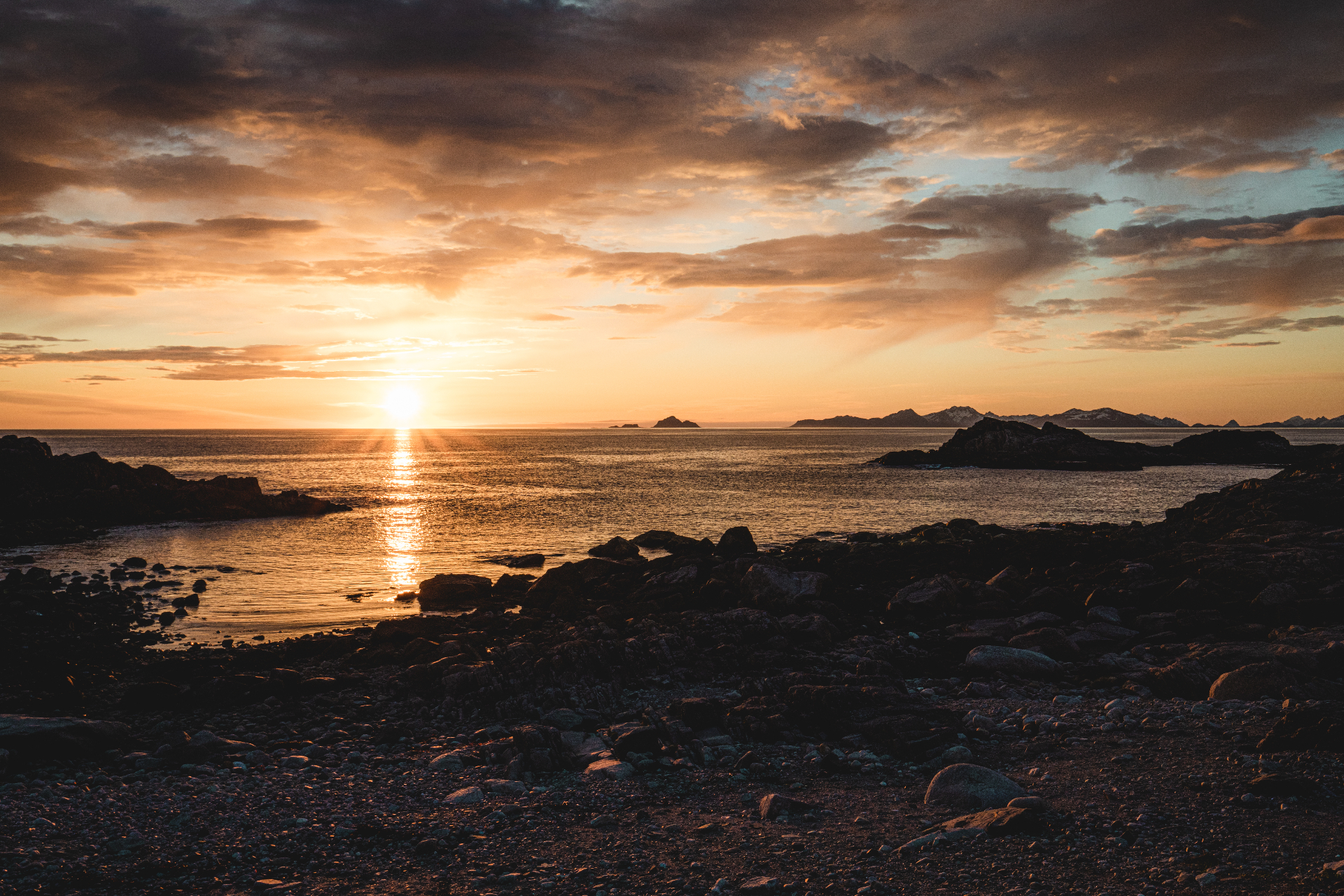 Golden midnight sun settling over a rocky Lofoten coastline and distant islands