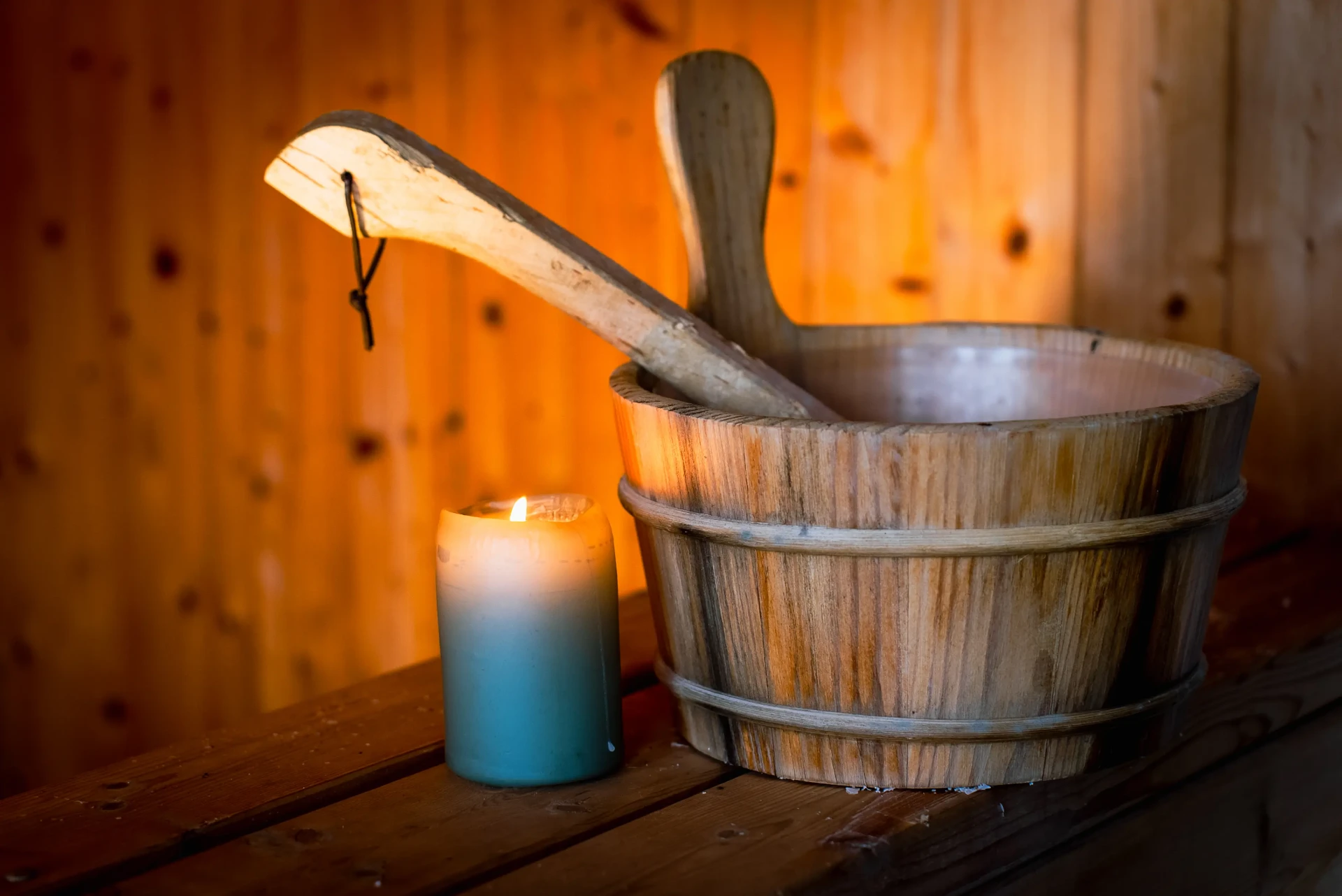 Wooden sauna bucket and ladle glowing beside a single candle on pine bench