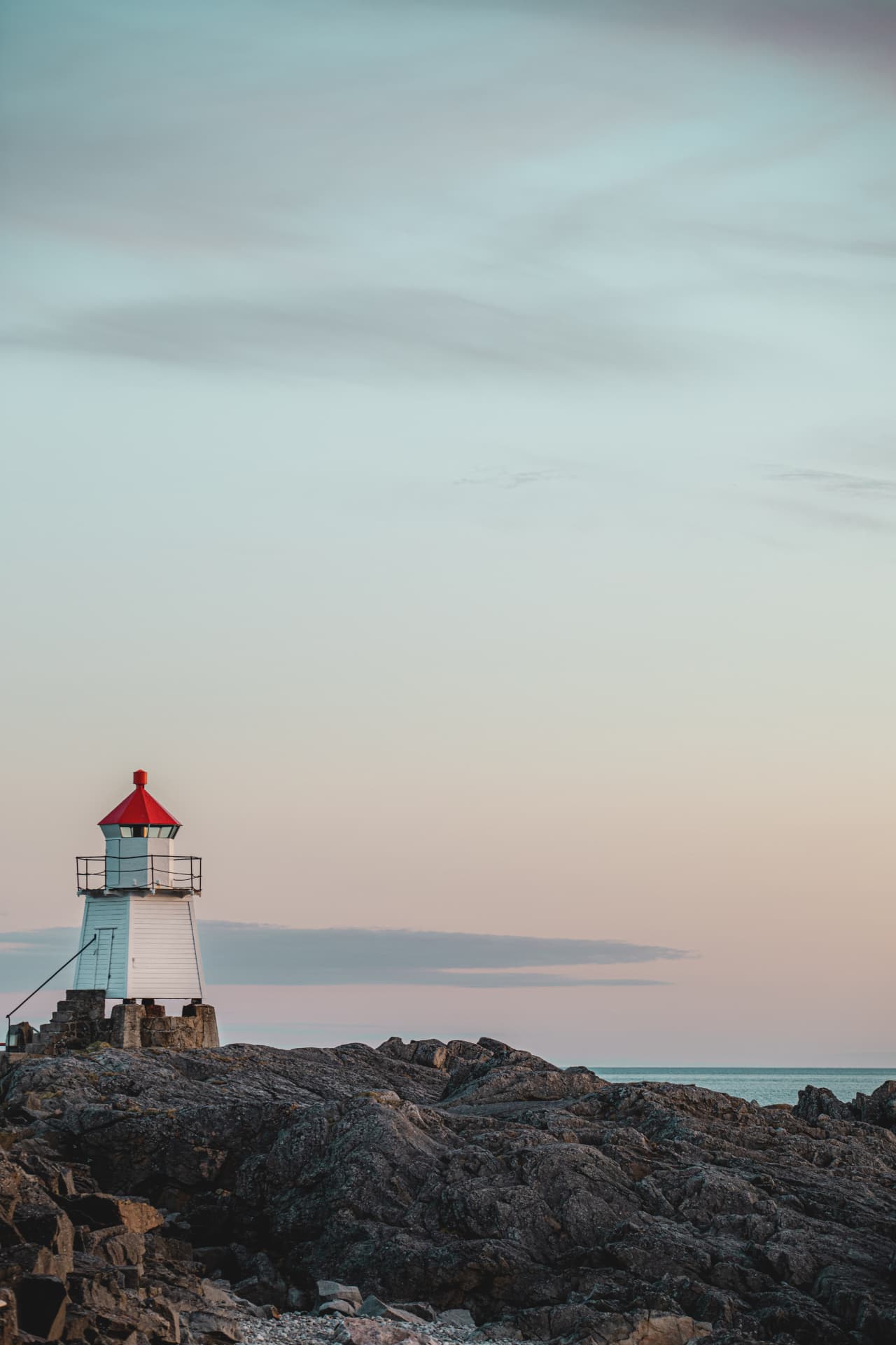 Small red-capped Lita Lykt lighthouse on bare granite in soft pastel dusk