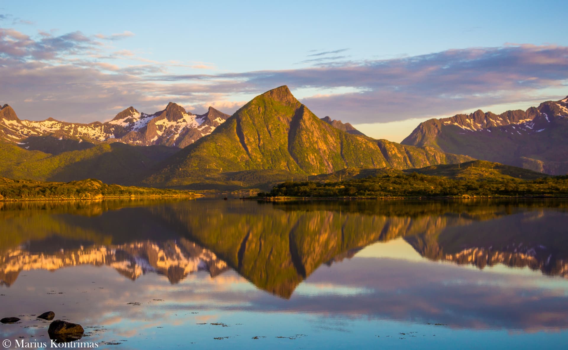 Still summer reflection of a green Lofoten peak mirrored in calm water at golden hour