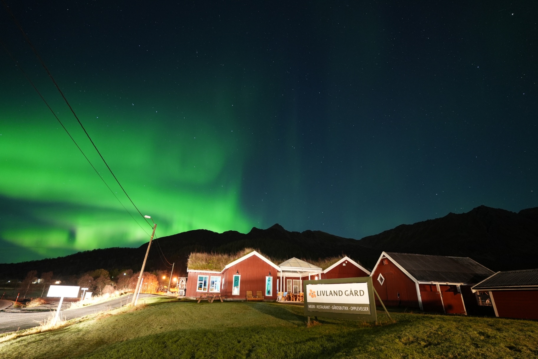 Livland Gård red turf-roof farm buildings under a bright green aurora and starry sky