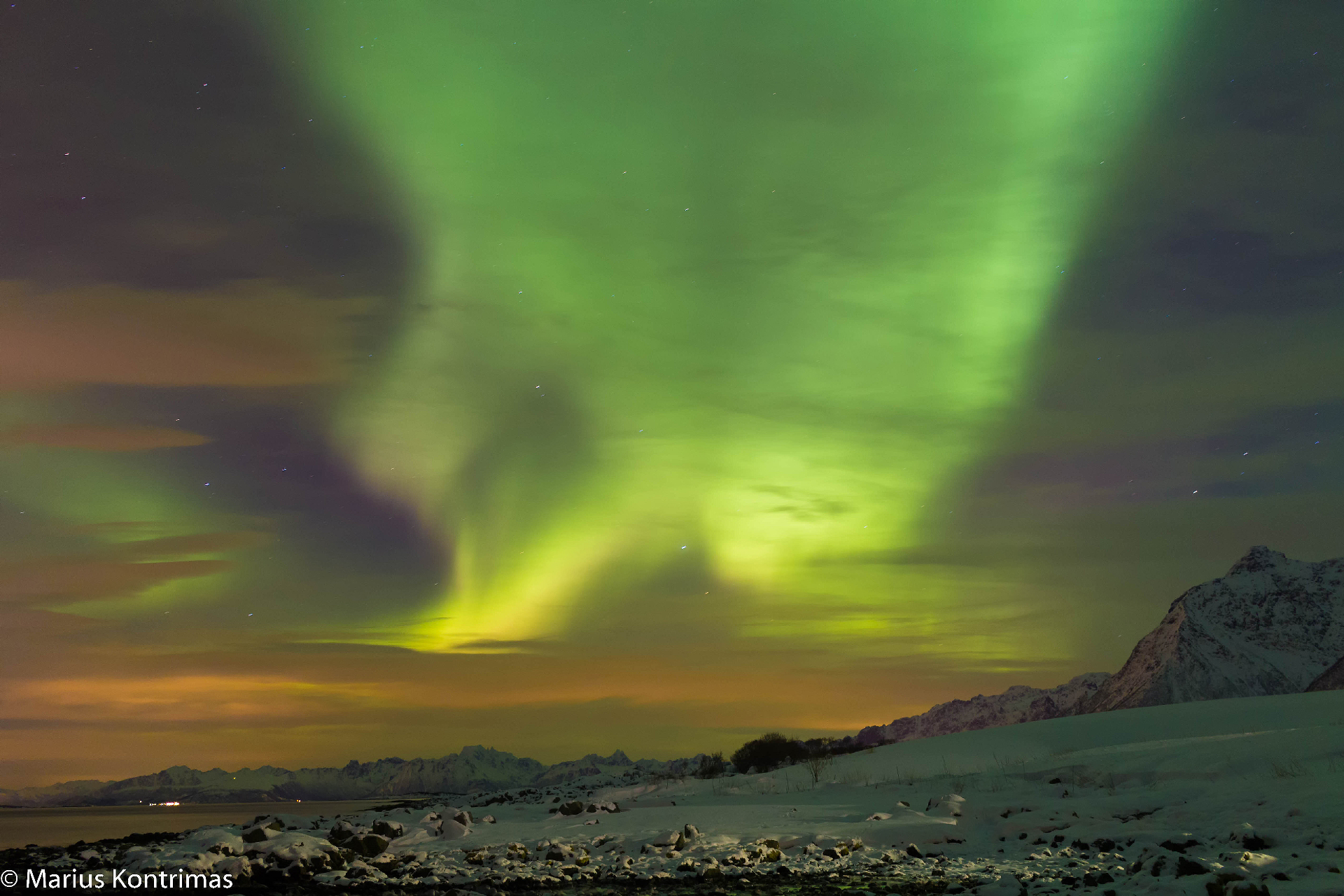 Aurora sweeping across the sky above snow-covered Lofoten peaks