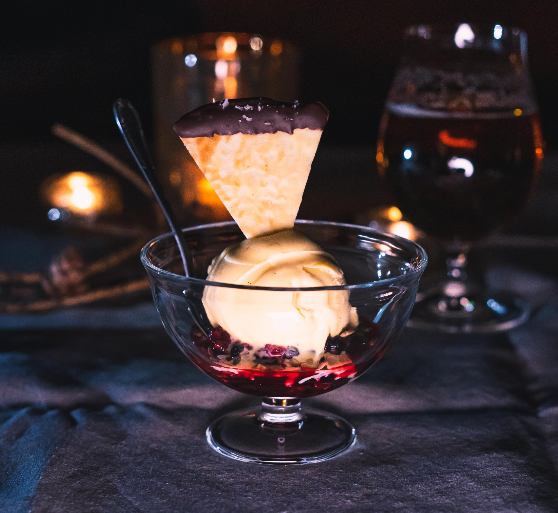 Dessert coupe with vanilla ice cream, berries and crisp biscuit in low candlelight