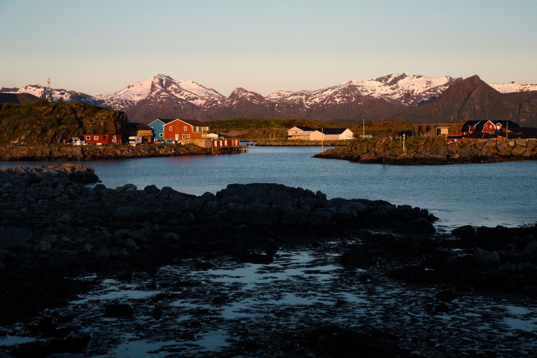 Red harbour cabins and snow-capped Lofoten peaks glowing in low midnight-sun light