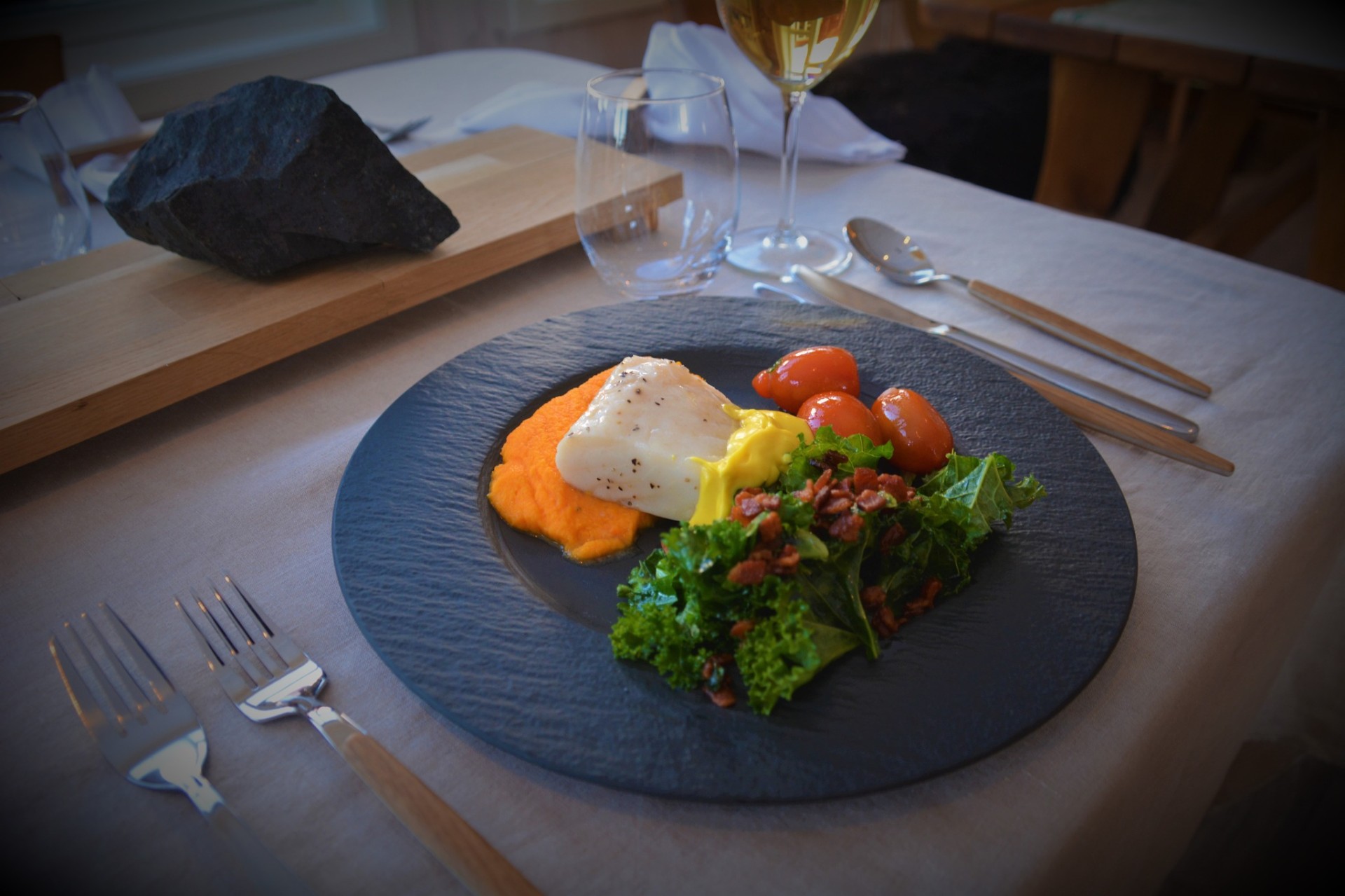 Refined plated cod course served on matte black stoneware with wine beside it