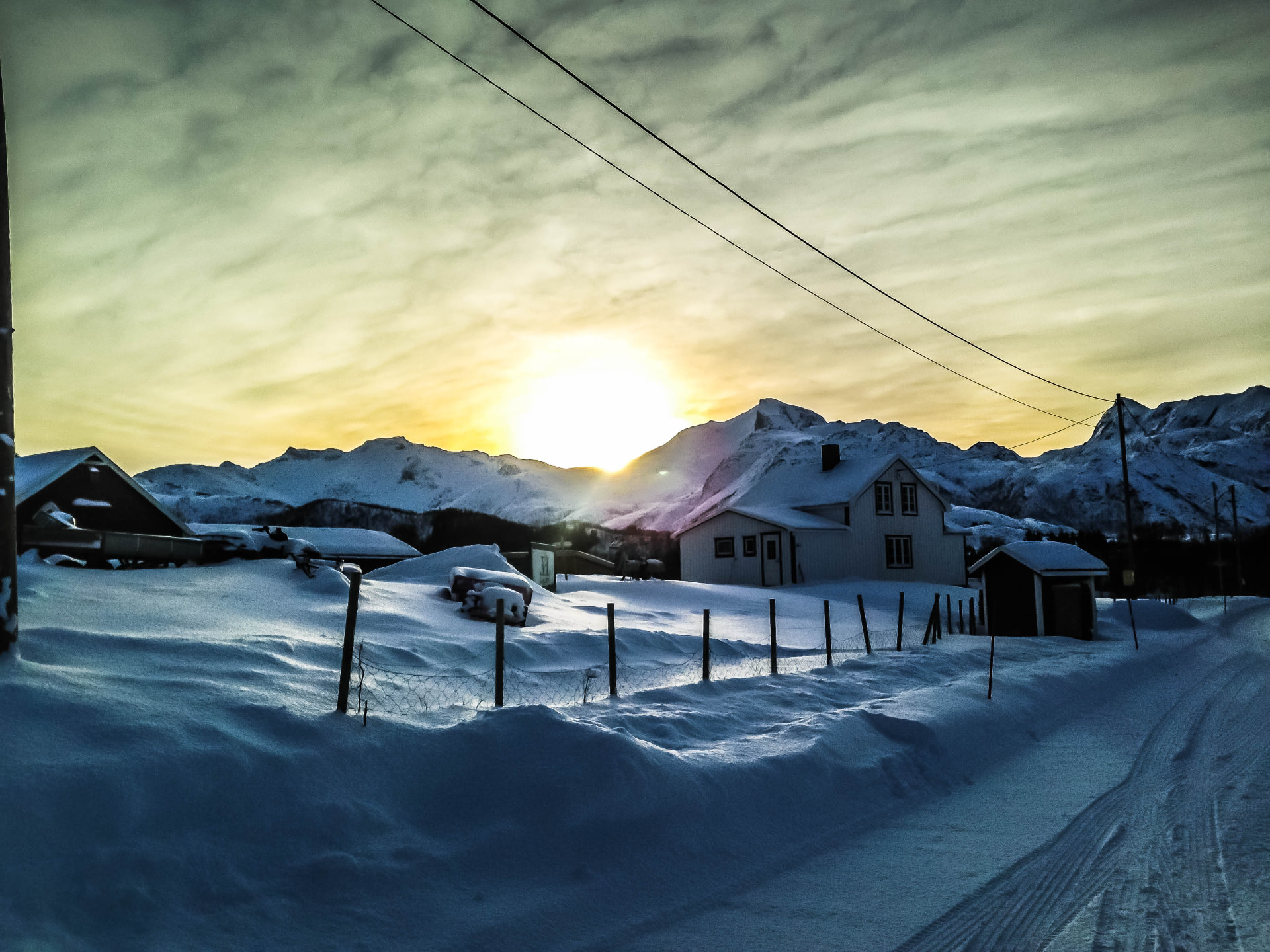 Winter sunrise behind a white farmhouse and deep snowdrifts in a mountain village