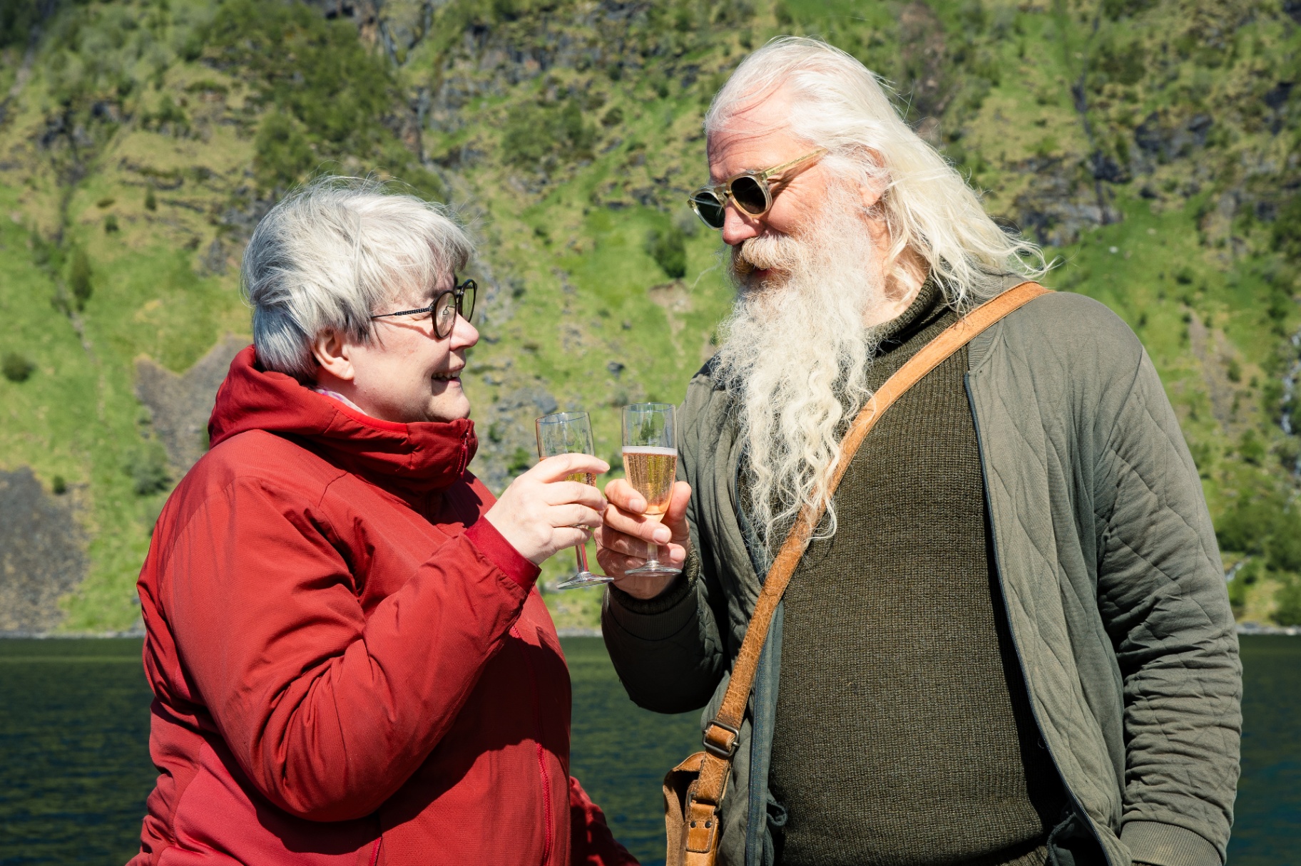 Guest and VISDI guide raising sparkling wine glasses beside a fjord in summer light