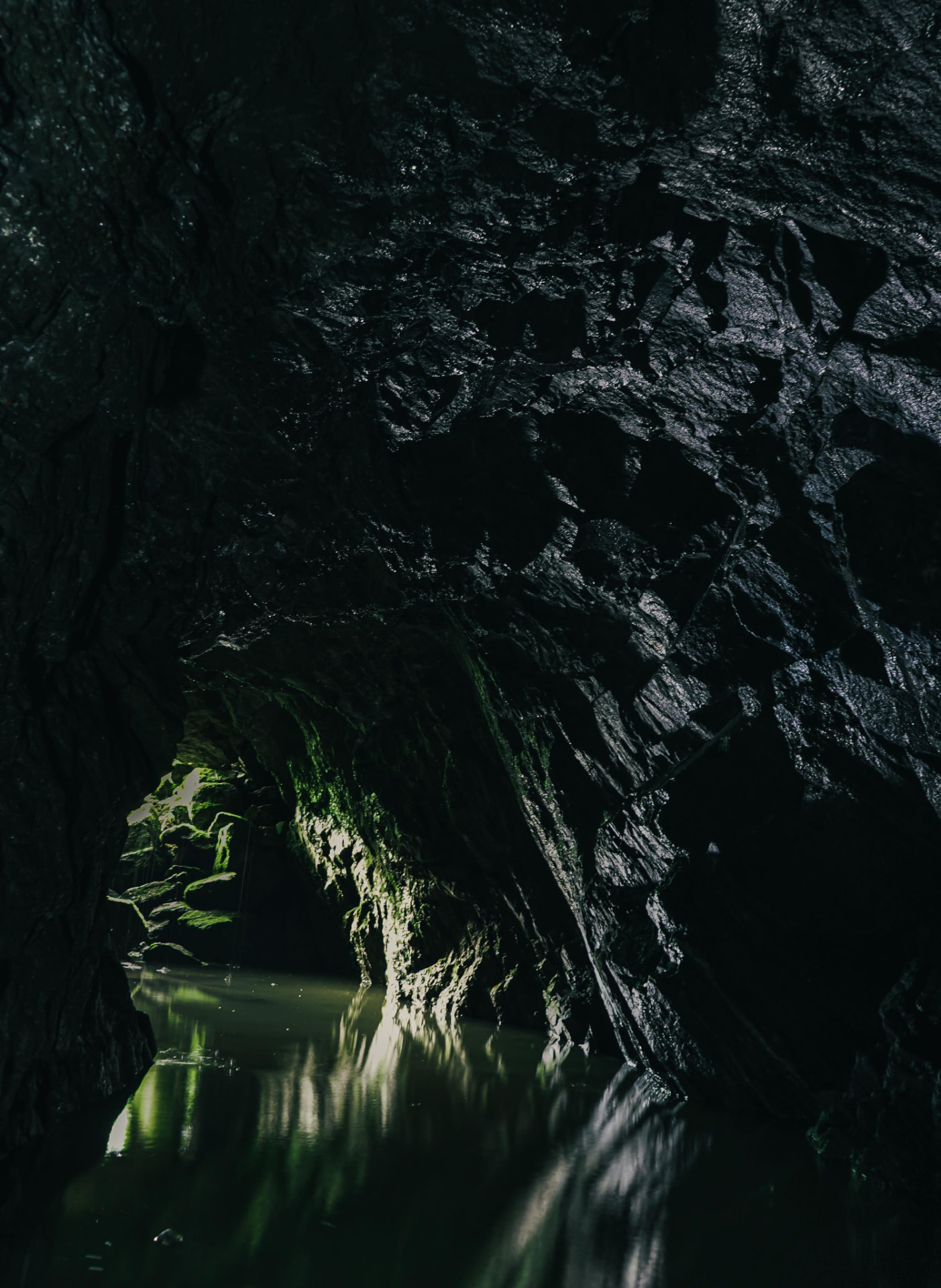 Water-filled mine adit at Matmora, wet rock walls opening towards a green shaft of daylight