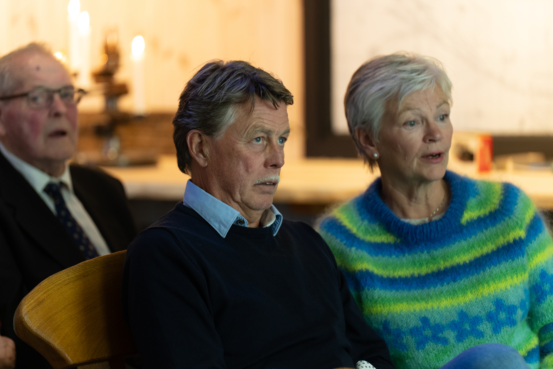 Three Lofoten locals listening and sharing stories in warm candlelight by an old lamp