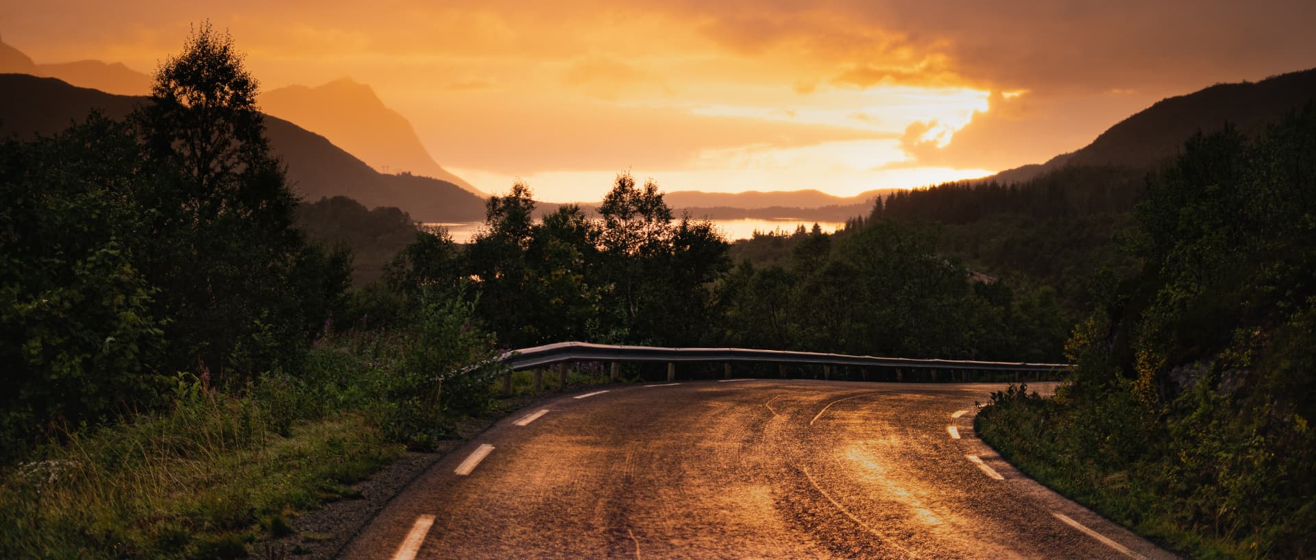 Winding Lofoten road at golden sunset with mountains and fjord in the distance